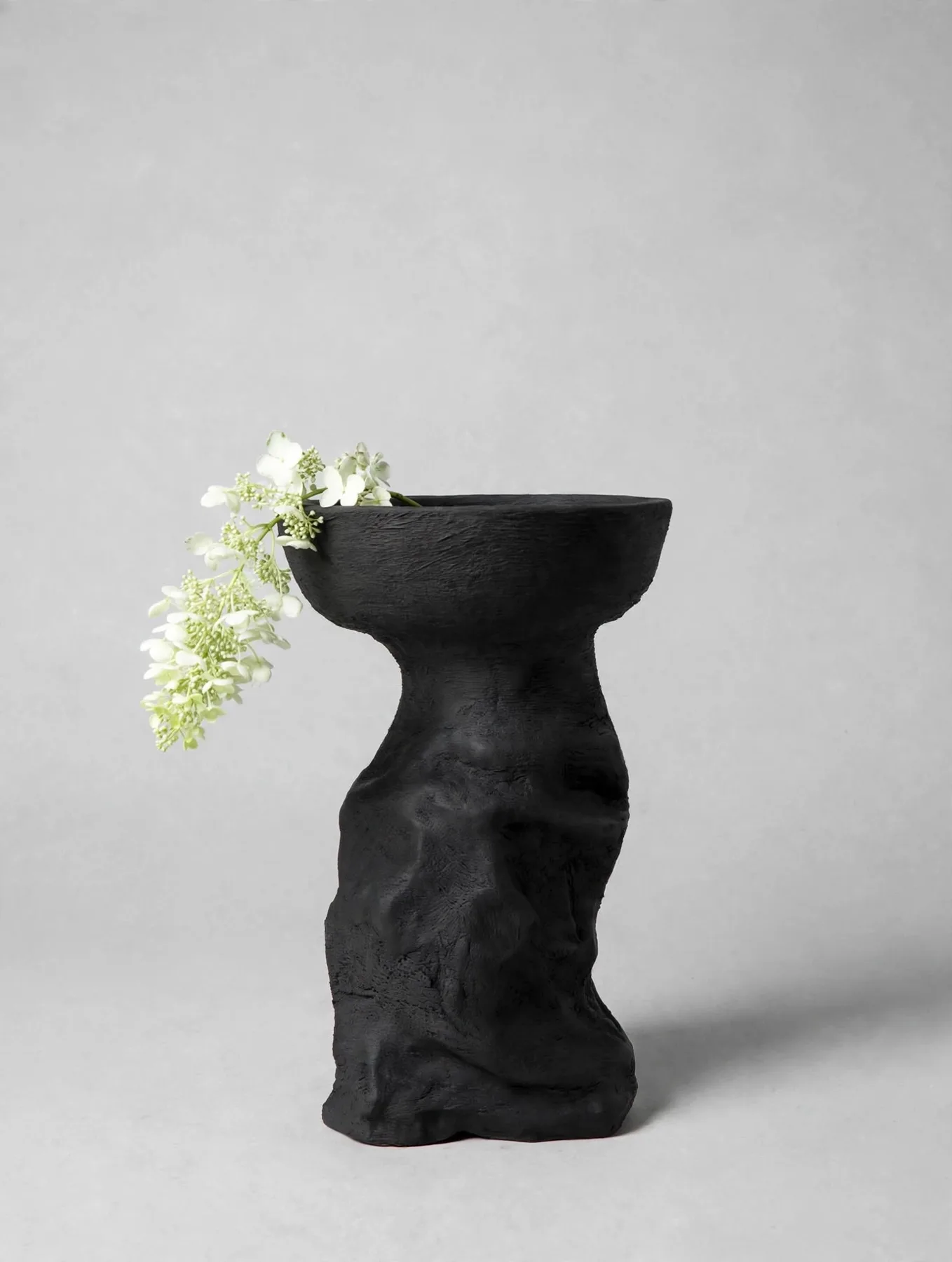 Black sculptural piece with a trailing stem of white hydrangea