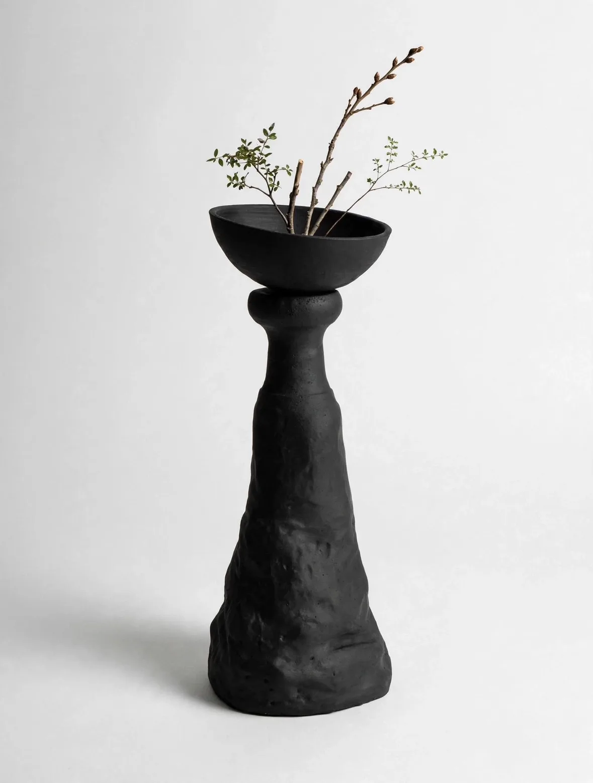 Tall black sculptural piece with a shallow bowl holding spring branches