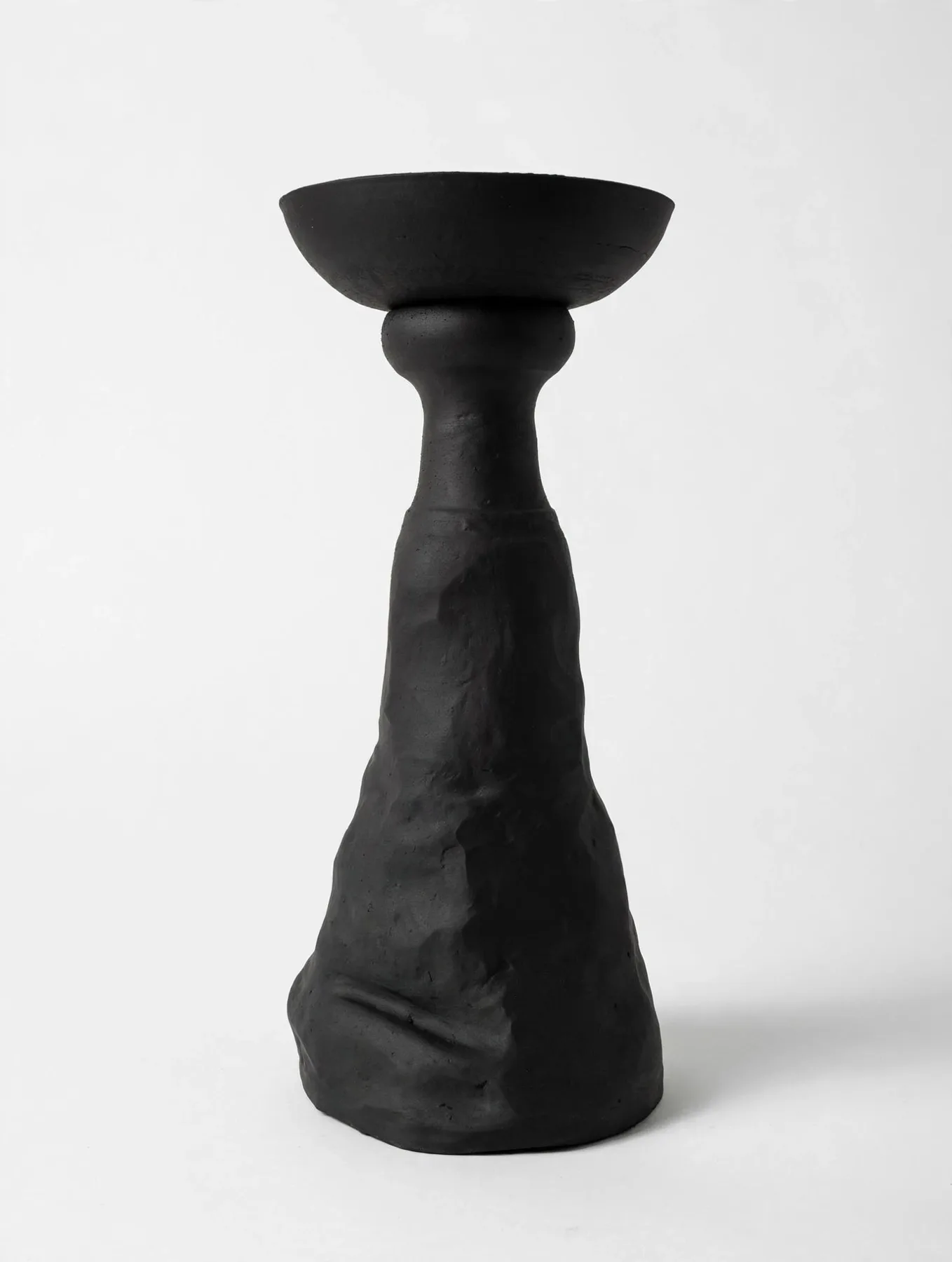 A tall black sculptural piece: a raw, hand-shaped base rising into a precise bowl